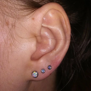 Three round opal ear studs in graduated sizes worn on ear with stainless steel base