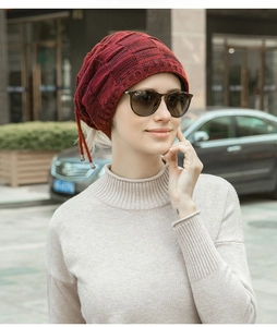 Dettaglio del berretto in maglia bordeaux con trama a griglia e cordoncino decorativo rosso