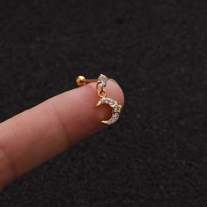 Macro shot of gold moon-shaped earring with zircon inlay held on fingertips