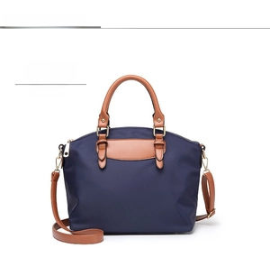 Detail view of navy nylon handbag with brown leather handles and adjustable shoulder strap