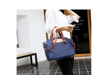 Detail of dark blue Oxford fabric bag with brown leather handles and gold zippers