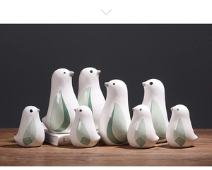 Nahaufnahme von Keramik-Vogelfiguren mit grünen Federfedern auf einem dunklen Holztisch