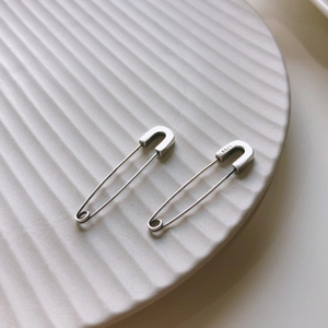 Macro shot of S925 sterling silver safety pin earrings on textured ceramic dish