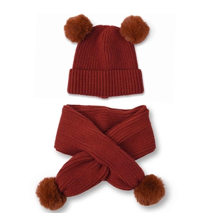 Detail of burgundy knit baby hat and scarf set with soft faux fur pom-poms for winter