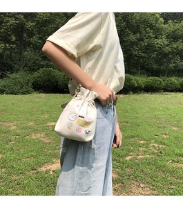 Outdoor shot of beige canvas drawstring bucket bag with cute cartoon prints and slogans