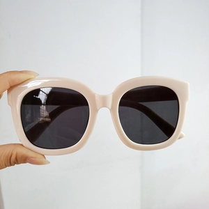Close-up of cream square frame sunglasses with dark gray lenses held by hand