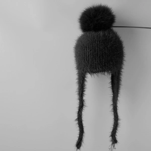 Detail of black faux fur knit hat with large pom-pom and protective long earflaps