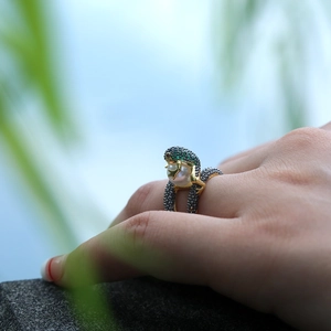 Detailed close-up of a frog-shaped 18k gold ring with green gems and a white pearl