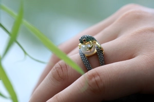 Macro detail of frog ring with white pearl, green gems, and 18k gold plating