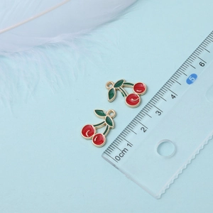 Macro shot showing exact size of 2.2cm red cherry charm with green leaves on scale