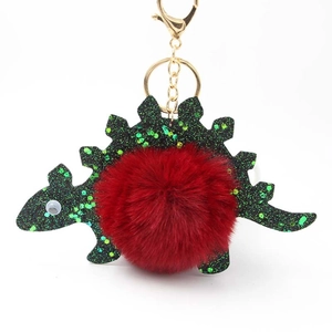 Detail of green glitter dinosaur keychain with a soft red pom-pom and golden clasp