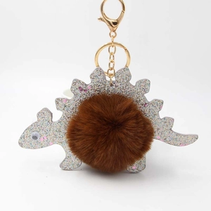 Detail of cute silver glitter dinosaur keychain with brown faux fur ball and gold clasp