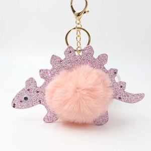 Detail of pink faux rabbit fur pom pom on a glittery purple dinosaur keychain with gold clasp