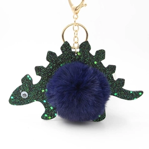 Detail of cute green sequin dinosaur keychain with fluffy navy blue faux fur pompom