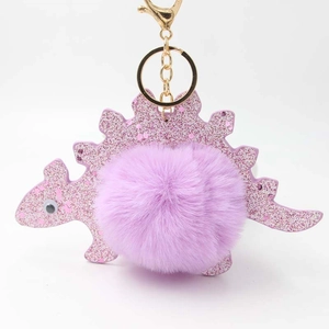 Close-up of a purple glitter dinosaur keychain with a soft fluffy plush pompom