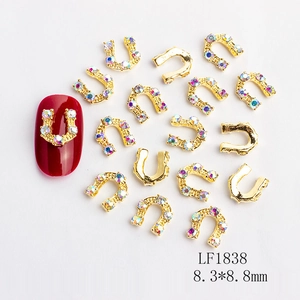 Golden horseshoe nail charms with rhinestones and U-shape design on deep red manicure