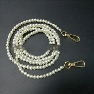 Detail of white round pearl strap with gold metal lobster clasps on a dark background