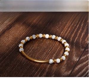 Detail of white marble beads and gold curved metal tube on a minimalist stretch bracelet
