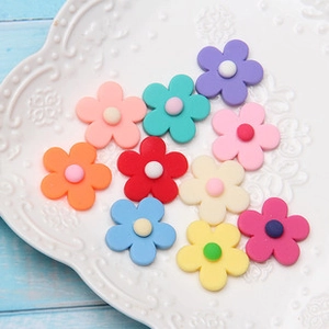 Colorful resin plumeria flower charms displayed on a white plate for DIY hair accessories