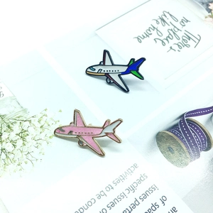 Pink glitter airplane enamel brooch and blue jet pin displayed on decorative background
