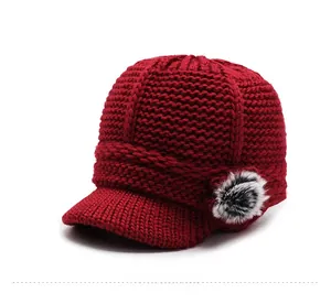 Detail of dark red knitted beanie featuring a brim and decorative side faux fur pompom