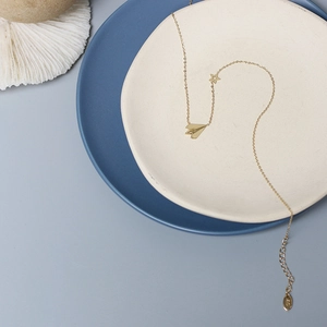 Close-up of gold paper plane and star pendant necklace on minimalist ceramic tray