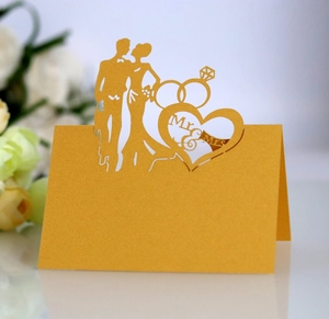 Close-up of laser-cut gold wedding place card with Mr & Mrs text and ring design