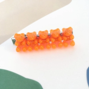 Detail of five translucent orange gummy bear charms on a silver metal hair clip