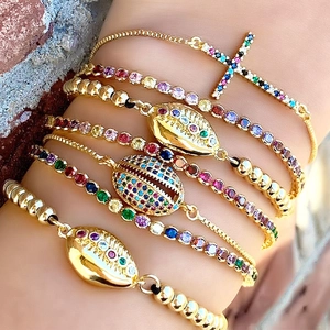Bracciali con strass arcobaleno con conchiglia e croce dorata sovrapposti sul polso