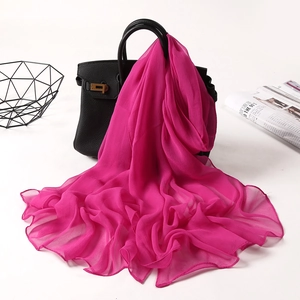 Detail showing a bright pink wavy edge chiffon scarf draped over a black handbag