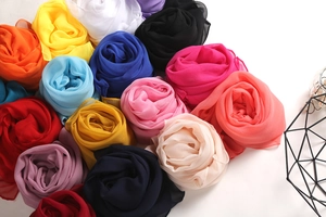 Detailed overhead view of multicolored lightweight georgette silk scarves in rose rolls