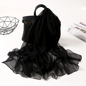 Lightweight black chiffon scarf draped elegantly over a black handbag on a white desk