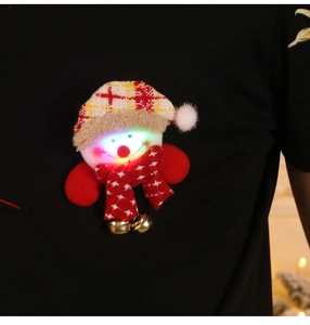 Detail of LED glowing snowman brooch with knit hat and golden bells on black fabric