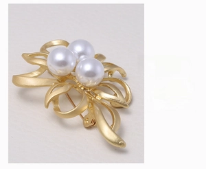 Macro shot of matte gold alloy brooch featuring three white pearls and sleek ribbon design