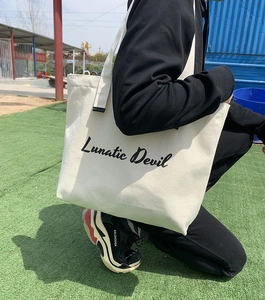 Close-up of a large off-white canvas tote bag featuring black Lunatic Devil artistic print