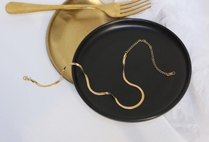 Detail of gold snake chain necklace with lobster clasp on a black matte plate