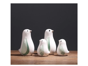 Set aus vier Keramik-Vogelfiguren in Creme und Grün auf Holzoberfläche vor grauem Hintergrund