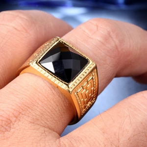 Detail of men's gold square ring featuring a large faceted black gemstone on model