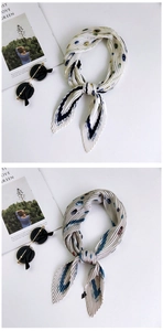 Detail view of cream pleated scarves with blue and green floral patterns and art cards