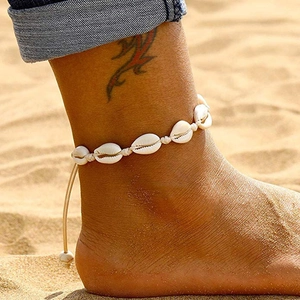 Bohemian anklet with natural white shells and beige woven rope on a sandy beach
