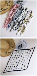 Flat lay of pleated square silk scarves in floral patterns with a straw hat and magazine