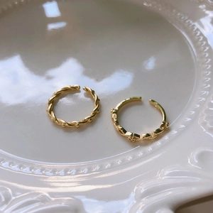 Detail of two gold adjustable rings with twisted rope and bead floral designs on white plate