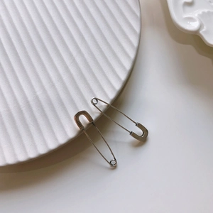 Detail of 925 sterling silver safety pin earrings on textured ceramic surface