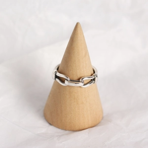 Detail of silver chain ring on wooden cone holder against white wrinkled paper