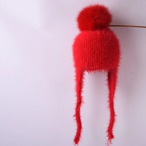 Detailed view of red knitted winter hat featuring a soft faux fur pompom and warm ear flaps