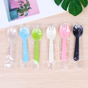 Disposable plastic sporks in assorted colors with individual wraps on wood surface