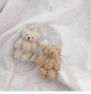 Close-up of white and brown curly plush bear keychains on textured fabric