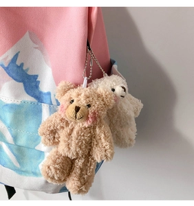 Close-up of light brown and cream plush bear charms hanging on a canvas backpack
