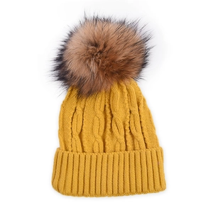 Detail of yellow knit beanie featuring thick cable patterns and a large fluffy fur pompom