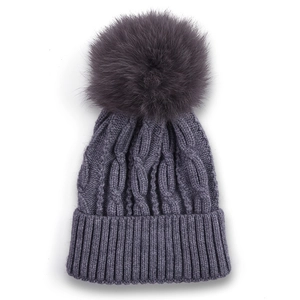Detail of grey cable-knit baby beanie featuring a fluffy faux fur pompom and ribbed cuff